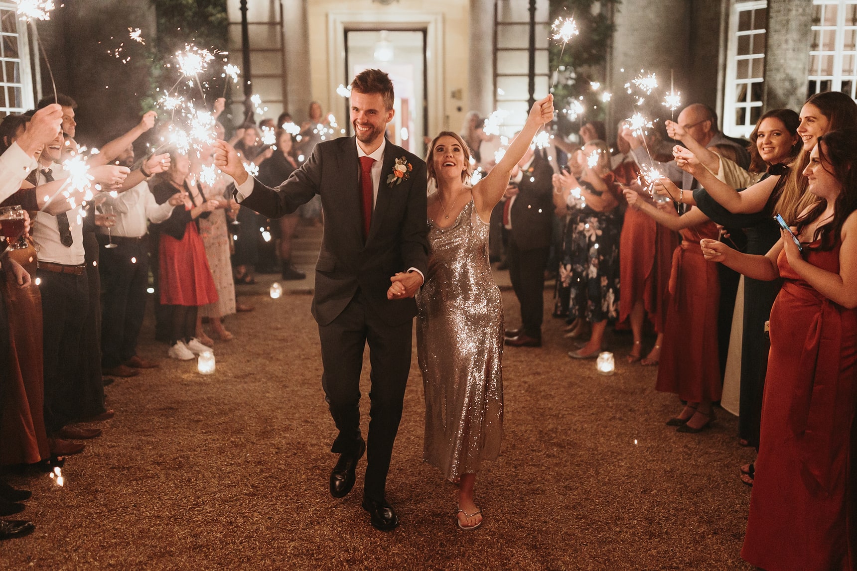 Bride and groom holding sparklers while walking through a sparkler archway