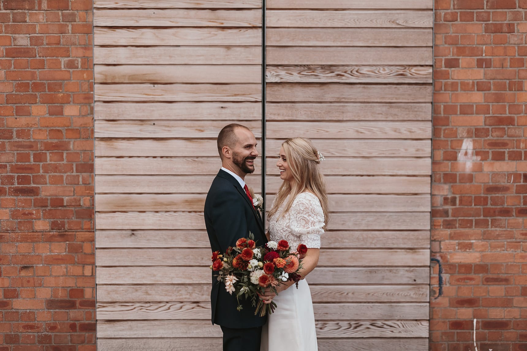 Wedding portrait of a bride and groom in front of a wooden door with bricks on the side