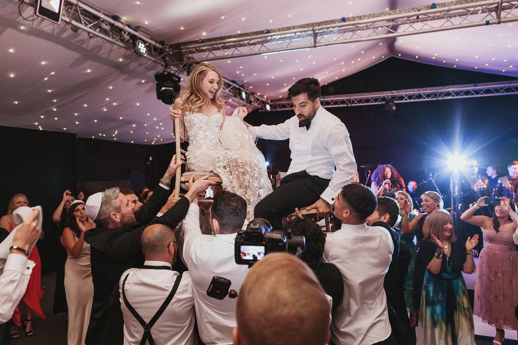 Jewish wedding with bride and groom been lifted on chairs