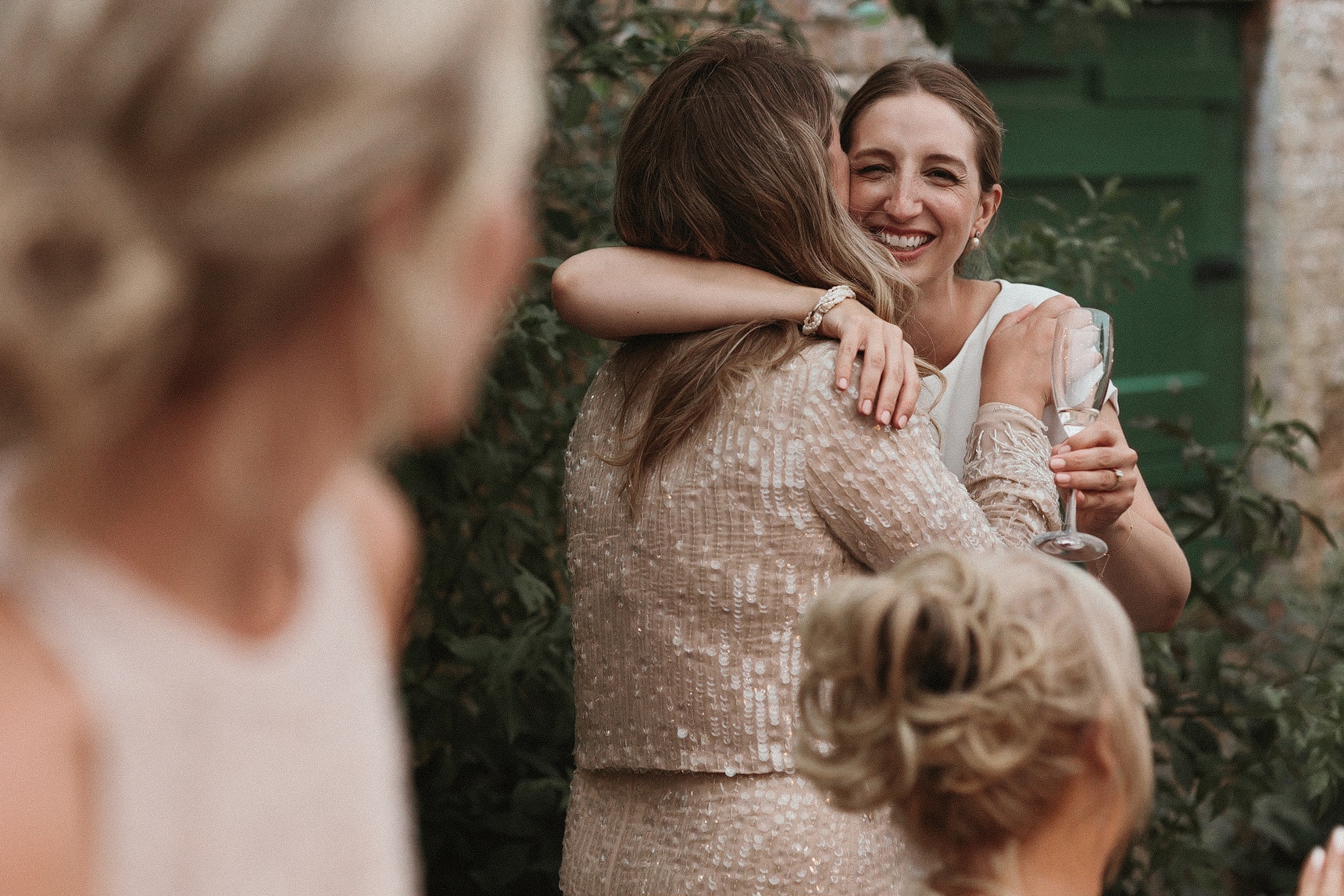 Bride with a glass of champagne in her hand and given her bridesmaid a hug with her free arm