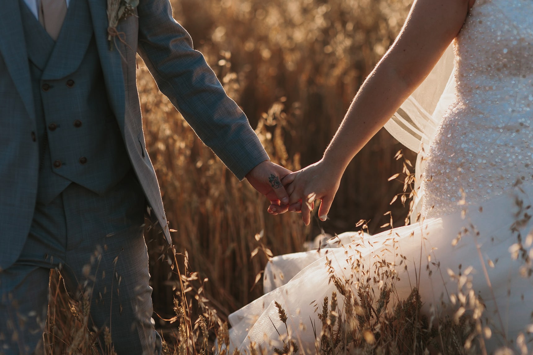 Bride and groom holding hands in a cornfield during sunset somewhere in Essex