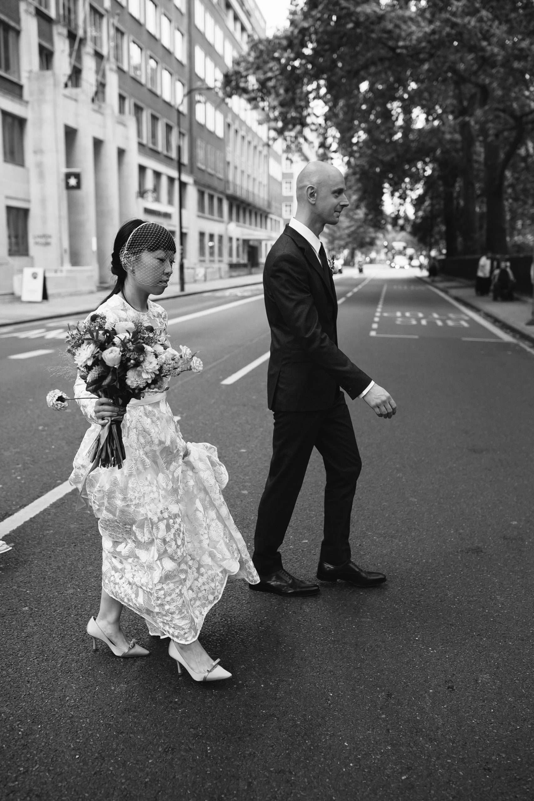 Black-and-white photograph of a bride and groom crossing the road in London